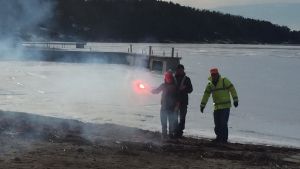 En flicka håller i ett flammande rött nödbloss på en strand med is på havet.