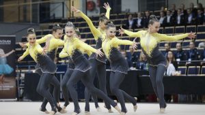 Aurora Kapanens lag Ovo Team i sina tävlingsdräkter. En grupp unga kvinnor i gul-grå gymnastikdräkter står i olika positioner