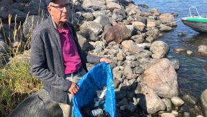 Dagens oimponerande fångst från Hattskär. En äldre man, Folke Österman står på en stenig strand. I hans händer är en stor kasse med plastskräp.