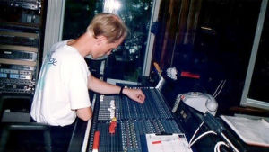 En ung Ridberg vid mixerbordet. Man med blont här och vit T-skjorta står vid mixerbord i musikstudio.