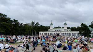 Hangö casino är en byggnad från 1800-talet som har fungerat som både casino och badhus. En bild på massor av människor som sitter på en strand och picknickar. I bakgrunden syns ett 1800-tals hus.
