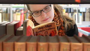 Kirjabloggari Niina Tolonen lukee kirjahyllyjen välissä Veijo Meren teosta.