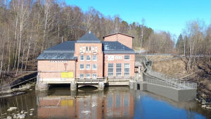 Bildmontage som visar den planerade fisktrappan i Åminnefors i Raseborg. Statliga stödpengar blev avgörande också för det bygget. Ett vattenkraftverk i rödtegel, till höger syns en byggd fiskväg. Bildmontage.