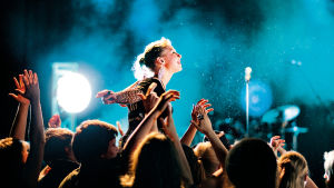 Yleisö taputtaa käsiään rock-konsertissa, yksi tyttö muiden yläpuolella.