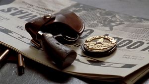 Revolveri koteloineen ja Los Angelesin poliisin virkamerkki makaavat pöydällä sanomalehden päällä. Kuva elokuvasta L.A. Confidential.