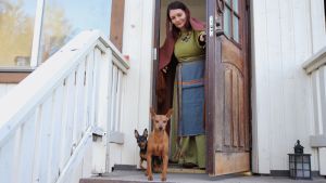 Mervi Pasanen kotiovellaan muinaispuku päällä. Etualalla kaksi koiraa.