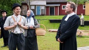 Nysto-Juck (Hans-Erik Ahlskog) och Nysto-Hulda (Fia Sundkvist) försöker slingra sig från prostens (Jan-Erik Enell) uppläxning om skriftskollungdomens velocipedande. Fabrikör Östenson (Matias Risikko) lyssnar i bakgrunden. två skådespelare står i gamla kläder med rynkande miner och lyssnar på en gammaldagsklädd präst i pjäsen frihetsdrömmar