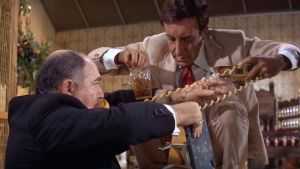 Hrundi V. Bakshi (Peter Sellers) auttaa juhlien isäntää (Stephen Liss) puhelimen johdon kanssa elokuvassa Pahuksenmoiset pirskeet