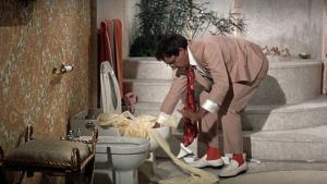 Hrundi V. Bakshi (Peter Sellers) on vaikeuksissa epäkuntoisen vessanpöntön kanssa elokuvassa Pahuksenmoiset pirskeet
