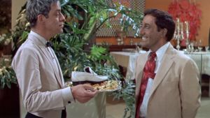 Hrundi V. Bakshi (Peter Sellers) saa kadonneen kenkänsä takaisin alkupalatarjottimella elokuvassa Pahuksenmoiset pirskeet