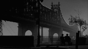 Isaac ja Mary (Woody Allen ja Diane Keaton) istuvat puistonpenkillä selin kameraan katsellen valaistua siltaa. Kuva elokuvasta Manhattan