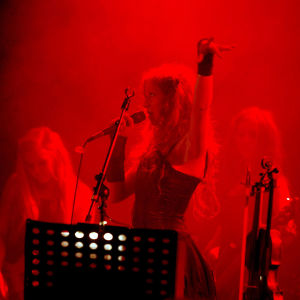 Indica-yhtye esiintyy punaisessa valossa. Etualalla laulaja Jonsu mikrofoni kädessä, toinen käsi ilmassa.