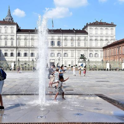 Turister svalkar sig i fontänen på ett torg i Torino i Italien