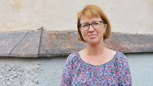 Hemvårdskoordinator Nina Lehtola. En medelålders kvinna i blommig blus står framför ett gulrappat hus. Hon ser in i kameran och ler.
