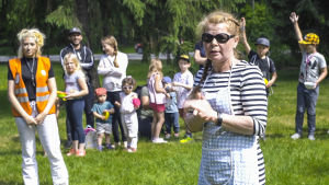 Lekparken Intia brukar få ungefär 120 besökare per dag till sin parklunch. Anneli Bäckström står på en gräsmatta i lekparken Intia i Forsby och leder en grupp barn.