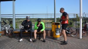 Drickapaus i Gammelby. Tre cyklister har matpaus i Gammelby. De sitter utomhus på en bänk.