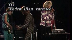 Kuvassa teksti "YÖ: Yhden illan varieteé" ja kolme yhtyeen jäsentä lavalla.