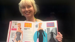 Utställningschef Minerva Keltanen håller i en stor bok om Barbiedockan. Utställningschef Minerva Keltanen håller i en stor bok om Barbiedockan.
