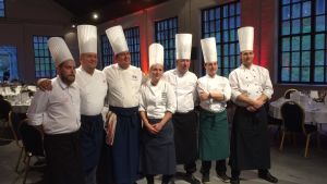 7 köksmästare har ordnat middagar runtom i Raseborg på olika restauranger. Här är de på Kuparipaja i Fiskars. Från vänster Micke Kokkonen Köttkontrollen, Kenneth Löfberg Åminne gård, Hasse Lundström GH-klubben, Emmi Retva Wärrsy, ”Weccu” Weckström Kuparipaja, Niko Tuominen Svartå slott och Uffe Wadenström KW. Nästa middag ordnas i april. Bild på sju krögare som har ordnat en middag. I bakgrunden syns dukade bord.