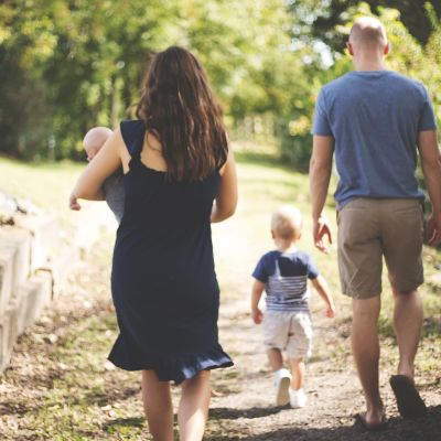 Mamma, pappa och två barn promenerar i en park.