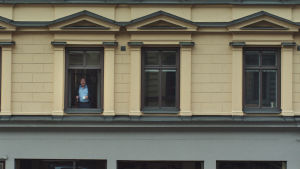 Välkommen till min värld. Roy Andersson i huset på Östermalm. Bild utifrån på Roy Andersson som står i ett av fönstren i huset där hans studio finns.