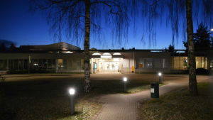 Borgå sjukhus. På bilden syns ingången till Borgå sjukhus om kvällen. Dörrarna finns på mitten av det avlånga huset. Den mörkblå kvällshimlen och några björkkvistar som hänger ner synns uppe på bilden.
