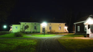 För tillfället ordnas bland annat läger och ungdomskvällar i Pernå prästgård. Det gula huset är den nyare prästgården medan det röda huset till höger är den gamla prästgården. Den står tom. Ett gult trähus på en gårdsplan i mörkret. Huset lyses upp av lampor på gården. Till höger syns en del av ett liknande rött trähus som står intilldet gula.