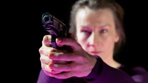 Huvudrollen Tova spelas av Elisabet Carlsson. Skådespelaren Elisabet Carlsson siktar med en pistol.