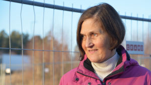 Monica Äikäs går ofta promenader i Majberget. En kvinna i pink jacka ler lite och tittar åt sidan. Solen lyser henne i ansiktet.