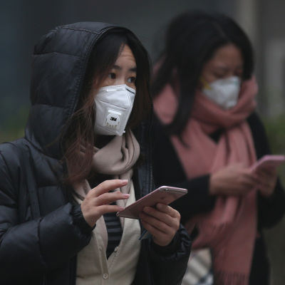 Två kinesiska kvinnor skriver på sina mobiltelefoner i utsläppsröken i Peking den 20 december 2016.