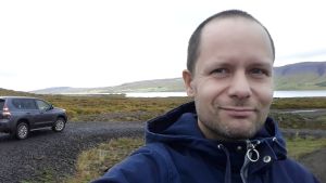 Tommi Lempinen ser inte med blida ögon på att Raseborg beslutat riva den gamla stockstugan. Tommi Lempinen utomhus vid ett vattendrag med en bil i bakgrunden.