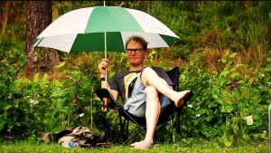 Harri Ojala istuu kentänlaidalla lukemassa kirjaa päivänvarjon kanssa.