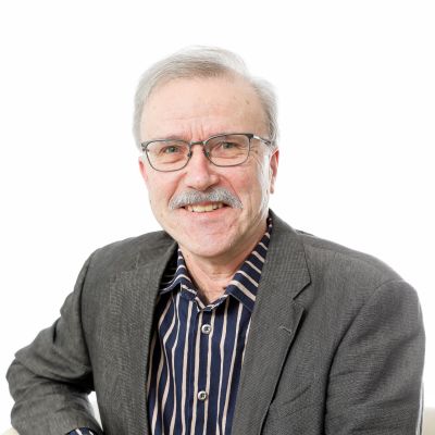 En man framför en vit bakgrund, han ser in i kameran och ser glad ut.