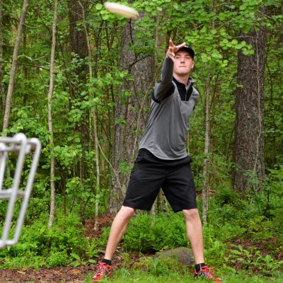 Mies heitää frisbeen kohti frisbeegolfkoria.