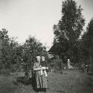 Vanhempi nainen nuori tyttö sylissään 1950-luvulla kaupunkipuutarhassa.