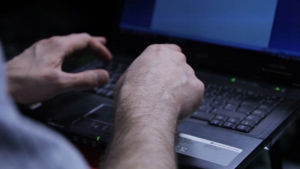 Två händer som skriver på en bärbär dator i halvmörker. 