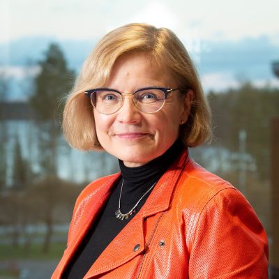 en medelålders kvinna i lederjacka och glasögon som ler mot kameran