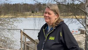 Nina Rönnberg tror inte att djuren saknar besökarna. "Men inte tror jag att de störs av att publiken kommer tillbaka." En kvinna i svart jacka med texten Korkeasaari Zoo med ett vattendrag i bakgrunden.