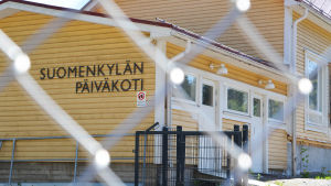 Ett gult trähus bakom ett stängsel. Det står Suomenkylän päiväkoti på väggen.
