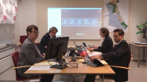 Fullmäktigemötet hölls per videolänk. Fyra personer sitter vid varsin dator runt ett bord. Bakom dem syns en stor skärm med olika mindre rutor.