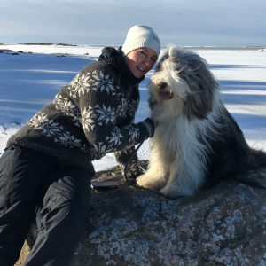 Patrica Strömbäck med sin hund på en sten vid en frusen strand.