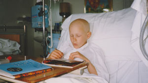 Aron var bara sju år gammal när han drabbades av cancer. Aron Anderson när han var cancersjuk som barn. Ligger i en sjukhussäng och läser.