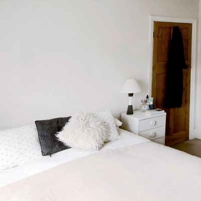 En dubbelsäng som är snyggt bäddad, ljusa färger, vit vägg, nattduksbord med lampa på båda sidorna.