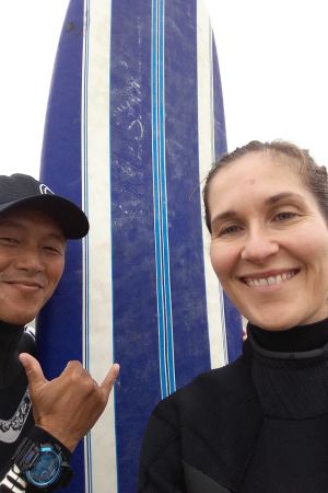 Surfmorgon med Sagawa, Katsuura, Japan 2016. Malin Kivelä, surfinstruktör och bräda. Bägge ler, han visar ett tecken med fingrarna.