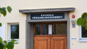 Svenska församlingshemmets vara eller icke vara har varit på tapeten många gånger. Senast år 2017 var det nära att fastigheten skulle ha satts ut till försäljning mot den svenska församlingens vilja. Arkivbild. Närbild på en gul byggnad. I mitten av bilden syns övre delen av en trädörr. Ovanför den står det Svenska församlingshemmet med versaler.