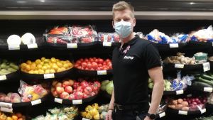 Toni Pohjoismäki, butikschef på Sale i köpcentret Rewell, tror vi kan vinna över coronapandemin. Mansperson står med munskydd på och tittar in i kameran. I bakgrunden fruktkorgar på rad i butikshylla.