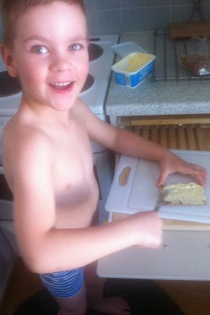 Pieni hymyilevä poika voitelee korppua keittiössä pelkät kalsarit jalassaan.