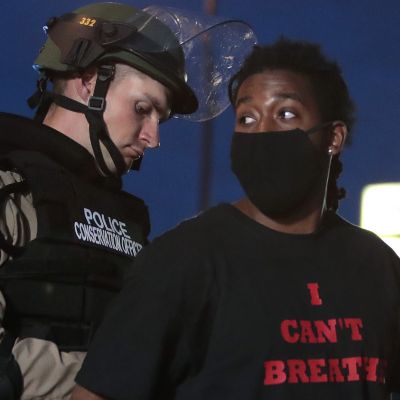 En polis sätter handklovar på en afroamerikansk kvinna som har en svart t-skjorta med texten "Jag kan inte andas".