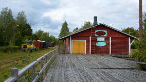 Tågspåret ligger strax invid Magasinboden. Till vänster tågspår och tågvagnar, till höger en röd träbyggnad med skylten Magasinboden.