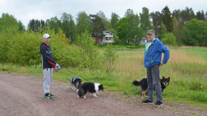 Harri Rantanen och Kari Kaukiainen är skeptiska till planerna. Två män och tre hundar står på en sandväg. Bakom dem syns träd och några hus.